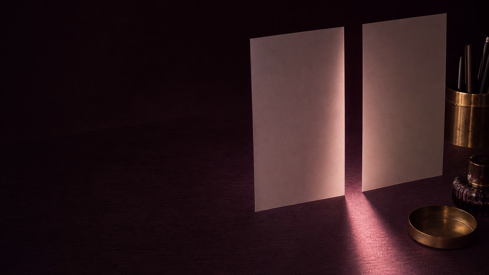 Two upright cream vellum sheets separated by a narrow path of rose light on a dark plum desk.
